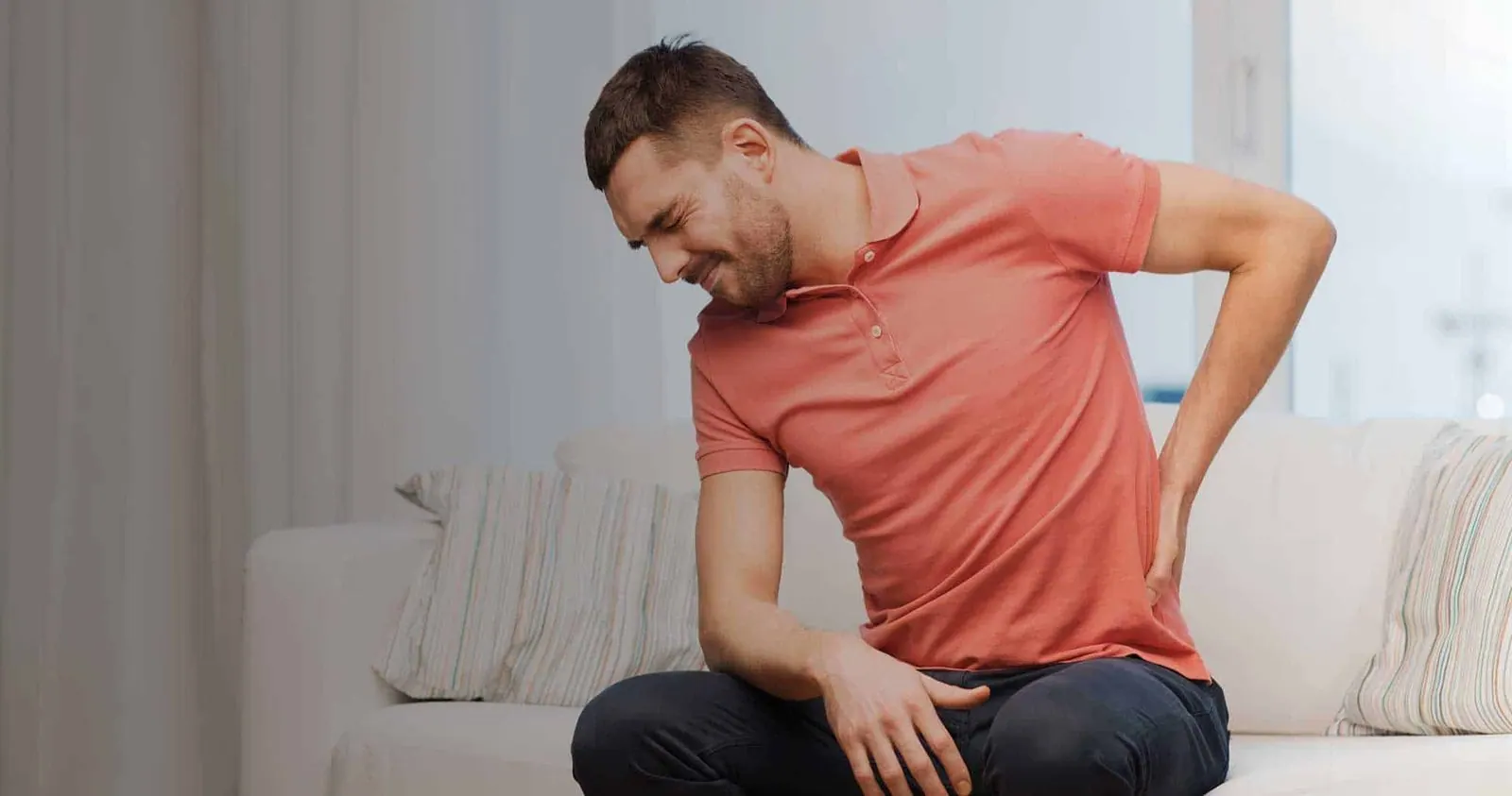 A man sitting at home holding his lower back
